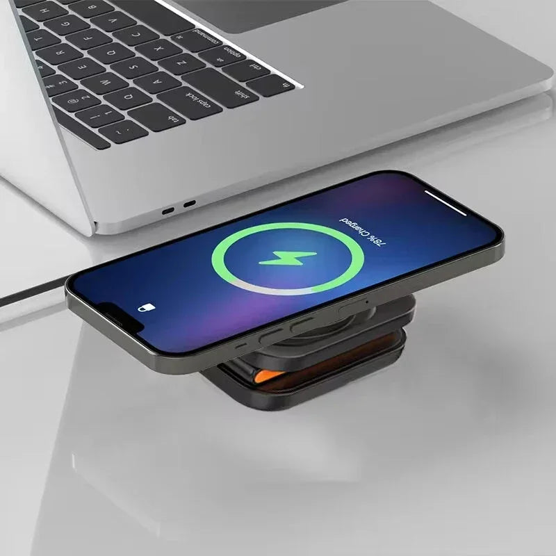 Wireless charging phone on compact charging pad next to laptop on glass desk