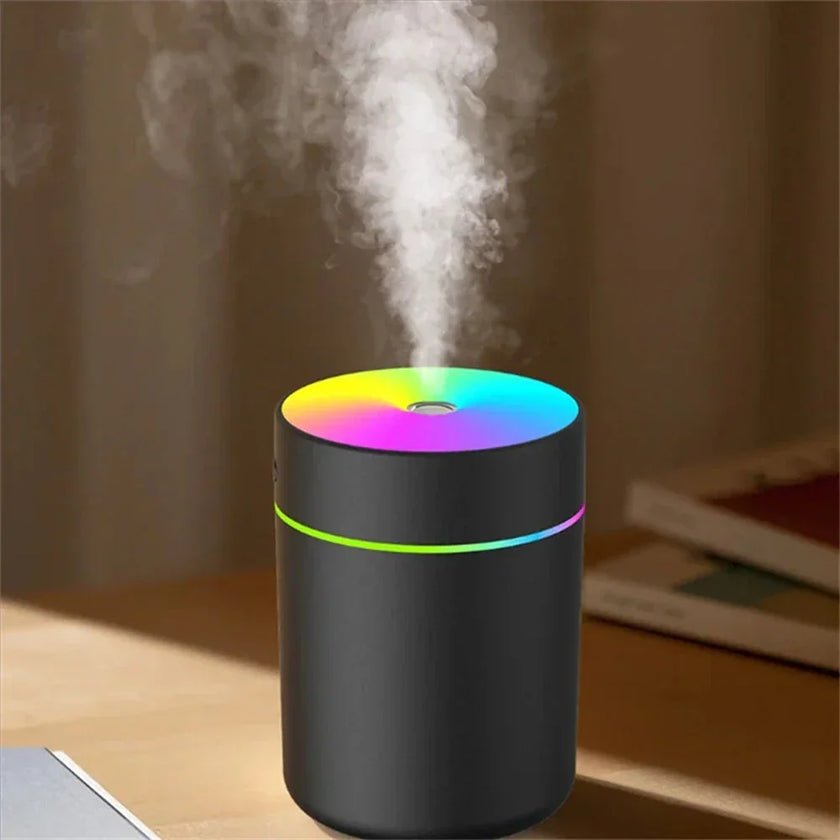 Black aroma diffuser with colorful LED light and visible mist on a wooden table indoors