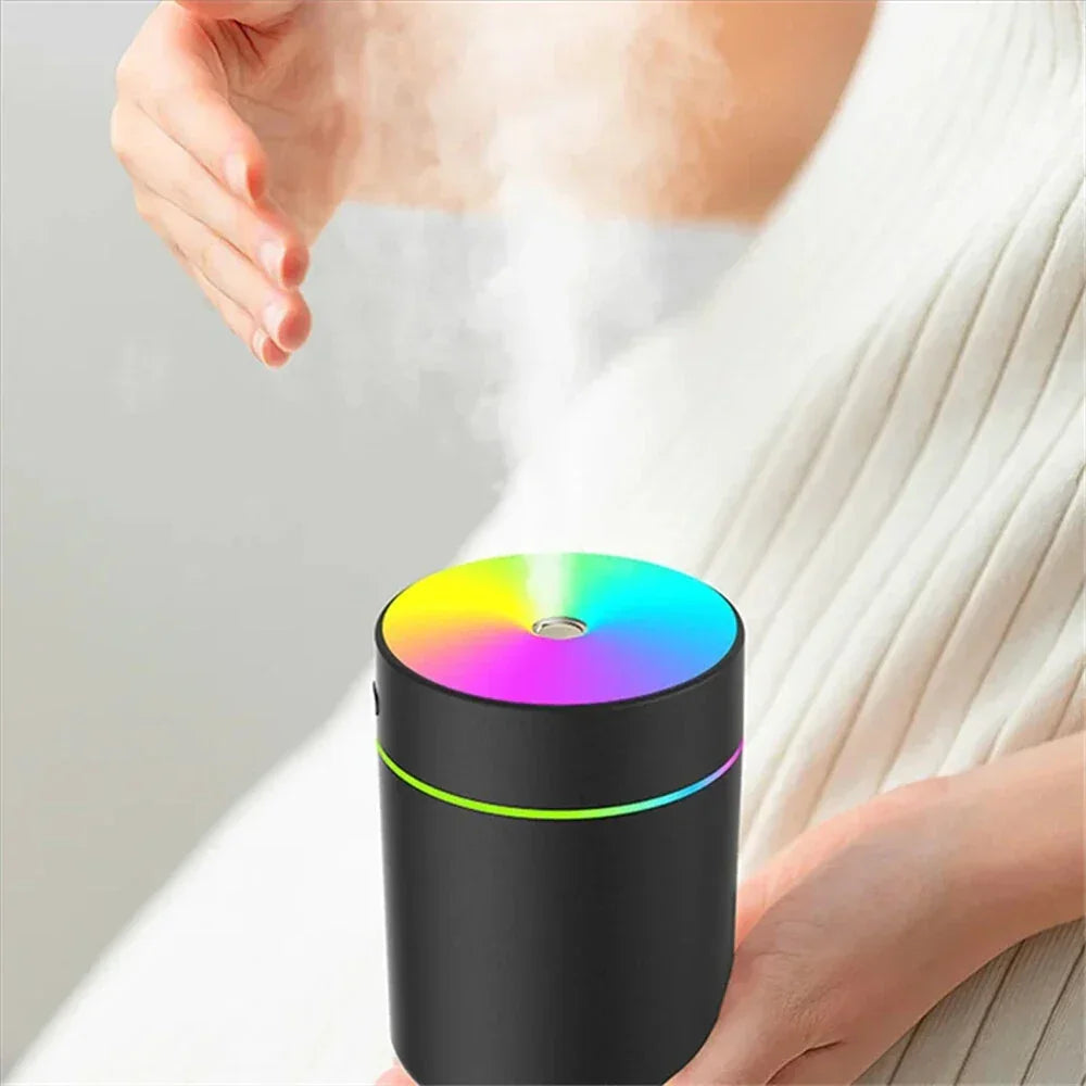 Hand over a black portable humidifier with rainbow LED lights releasing mist indoors