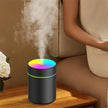 LED color aromatherapy diffuser emitting mist on wooden table near seated person