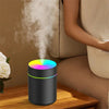LED color aromatherapy diffuser emitting mist on wooden table near seated person