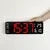 Hand adjusting large digital wall clock with red LED display on white background