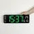 Large digital wall clock with green LED display mounted on white wall, hand adjusting