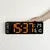 Hand holding digital wall clock with large orange LED numbers on white background