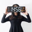 Woman in black dress holding large digital wall clock with calendar and temperature display