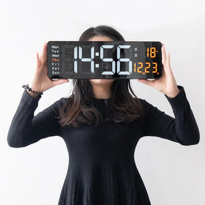 Woman in black dress holding large digital wall clock with calendar and temperature display