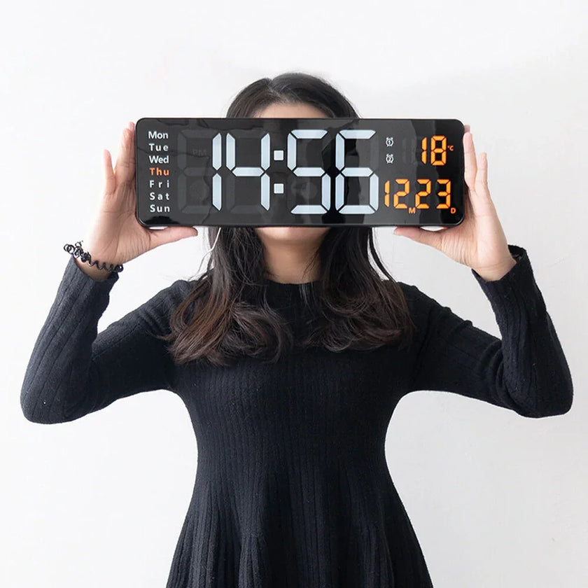 Woman in black dress holding large digital wall clock with calendar and temperature display