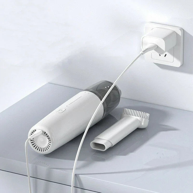 White portable handheld vacuum cleaner charging on tabletop with brush attachment