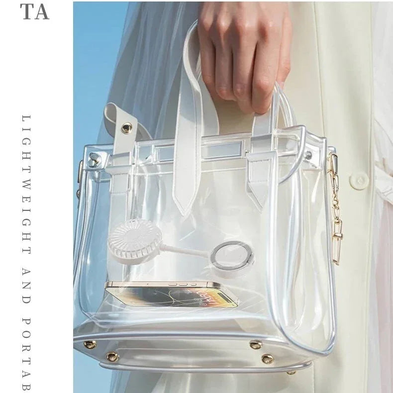 Woman holding a clear transparent handbag with white trim, phone, fan and accessories inside