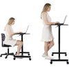 Woman using adjustable height desk workstation, sitting and standing with laptop on wheels