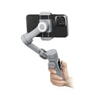 Hand holding gray smartphone gimbal stabilizer with phone mounted, white background