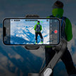 Hiker in green jacket filmed by smartphone on gimbal with snowy mountains background