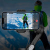 Hiker in green jacket filmed by smartphone on gimbal with snowy mountains background