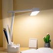 Modern white LED desk lamp on wooden study table with stationery holder, calendar, notebook, cactus decor