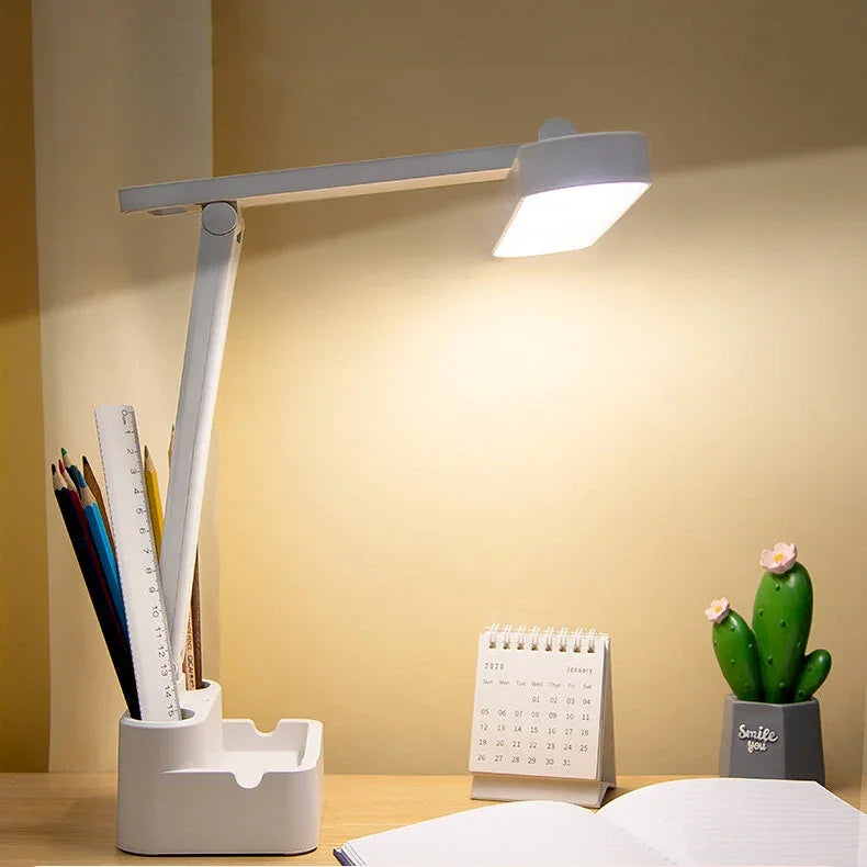 Modern white LED desk lamp on wooden study table with stationery holder, calendar, notebook, cactus decor